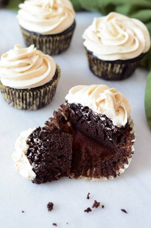 A few frosted chocolate cupcakes on a white table with one cut in half.