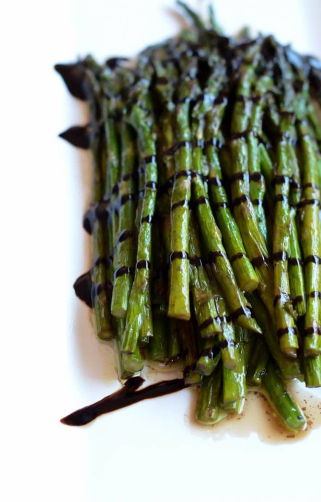 A close-up of a platter of roasted asparagus with a balsamic drizzle.