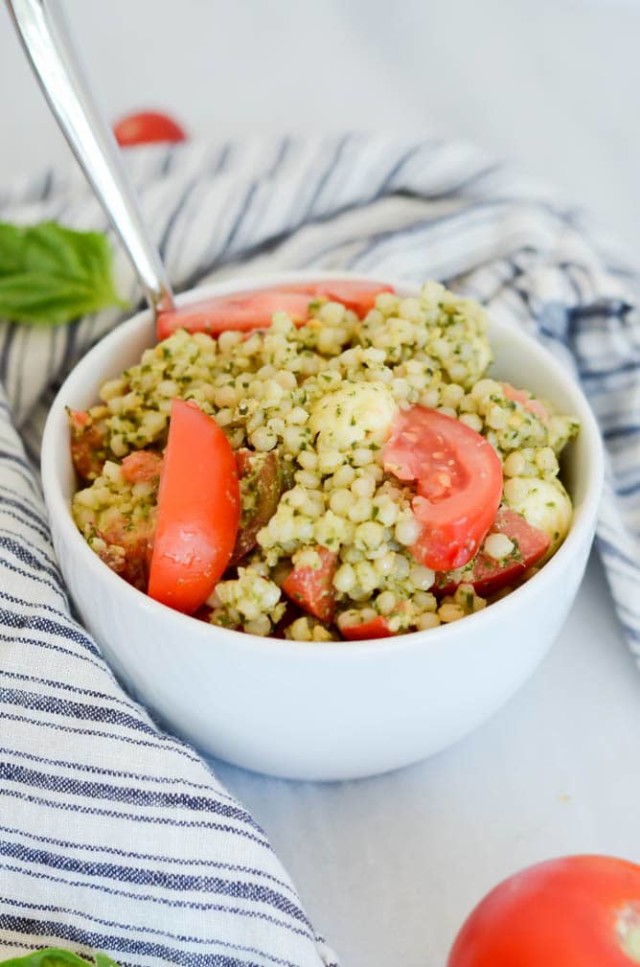 A bowl full of Hazelnut Pesto Caprese Couscous with a spoon.