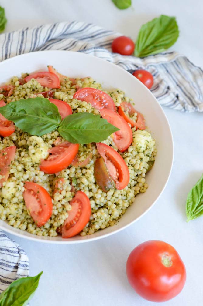 A bowl of hazelnut pesto couscous surrounded by fresh tomatoes and basil.