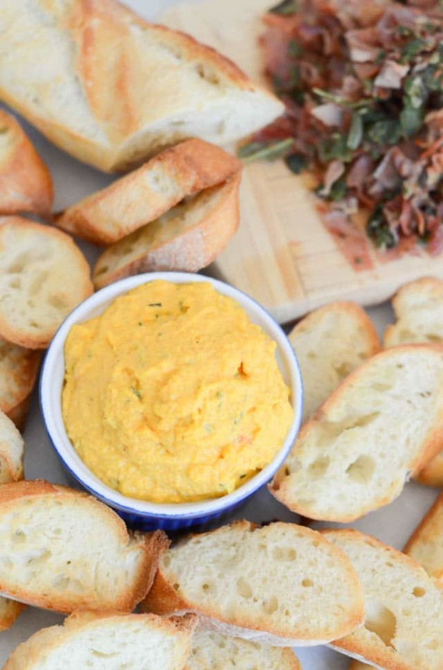 A dish of butternut squash spread surrounded by crostini and a pile of crispy prosciutto and sage.