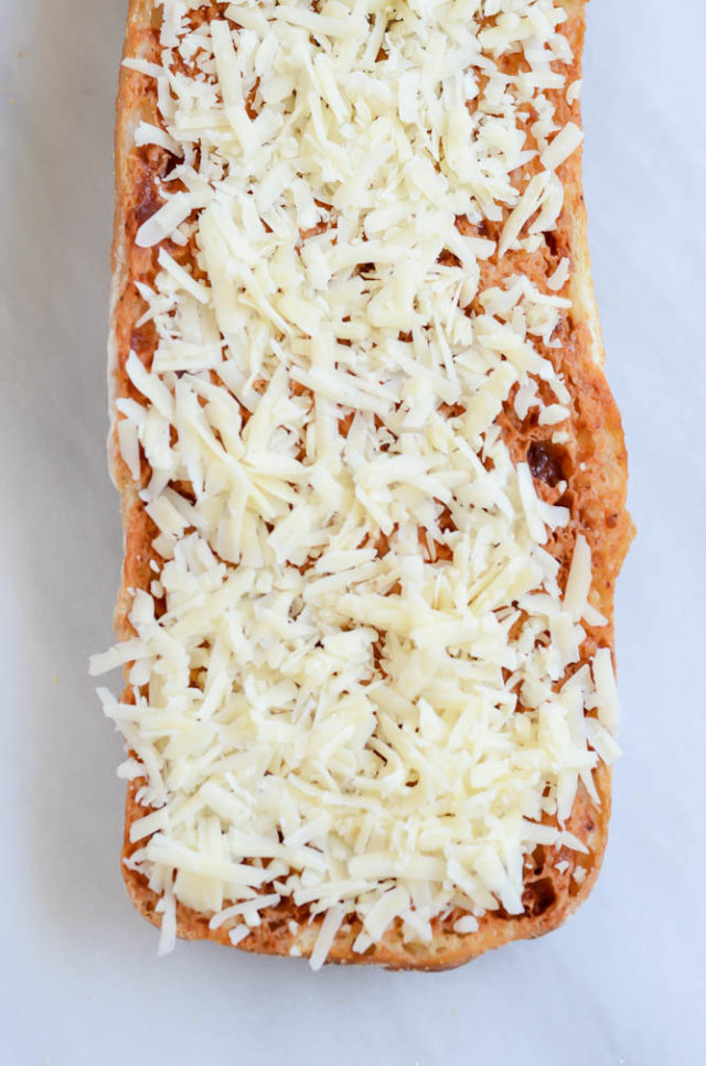 The second step to make Cheesy BBQ Garlic Bread - slather it with cheese!