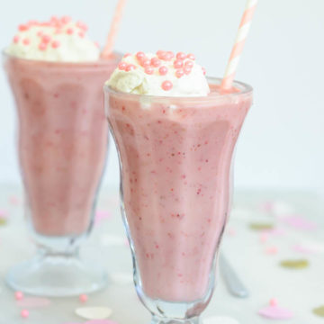 Profile view of frosty Lightened Up Double Strawberry Milkshakes topped with homemade whipped cream and pink sprinkles.