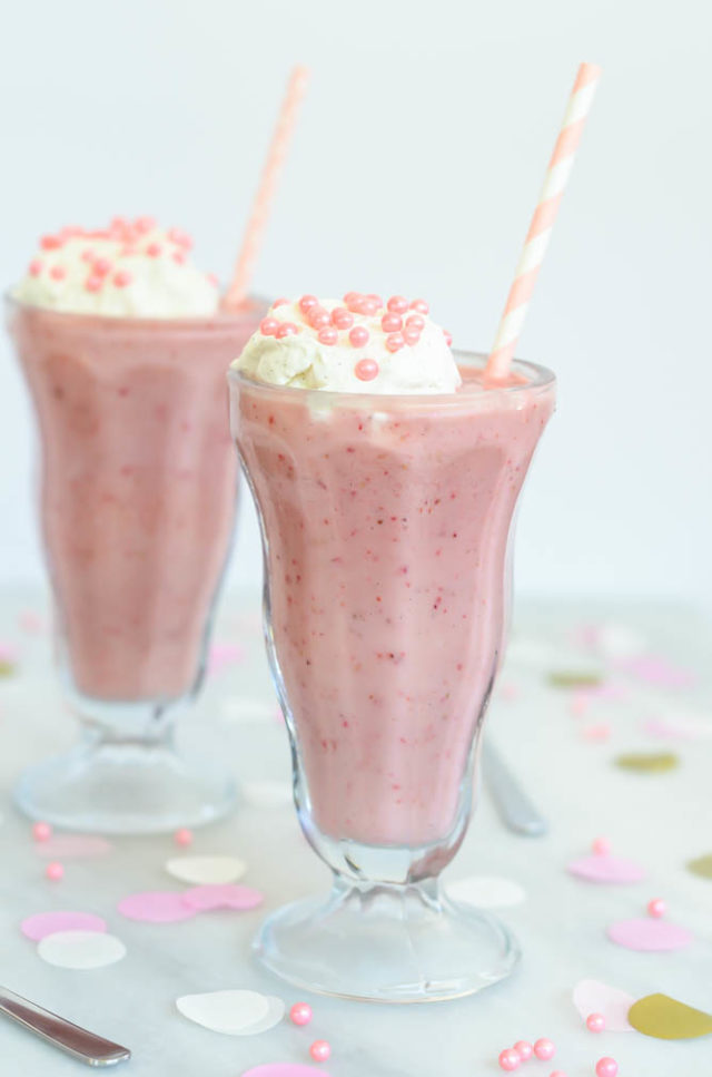 Profile view of frosty Lightened Up Double Strawberry Milkshakes topped with homemade whipped cream and pink sprinkles.