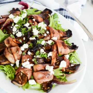 A large serving platter of Bacon-Wrapped Portobello Mushrooms with Goat Cheese over a bed of mixed greens.