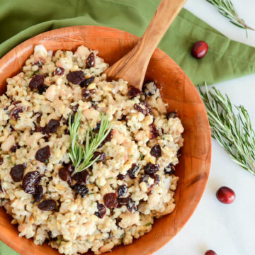 A bowl of Cranberry, White Bean and Grain Salad surrounded by a green linen napkin and fresh cranberries.