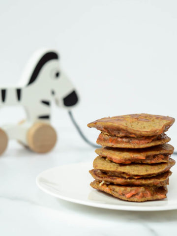 A stack of Healthy Carrot Cake Pancakes with a wooden zebra pull toy behind it.