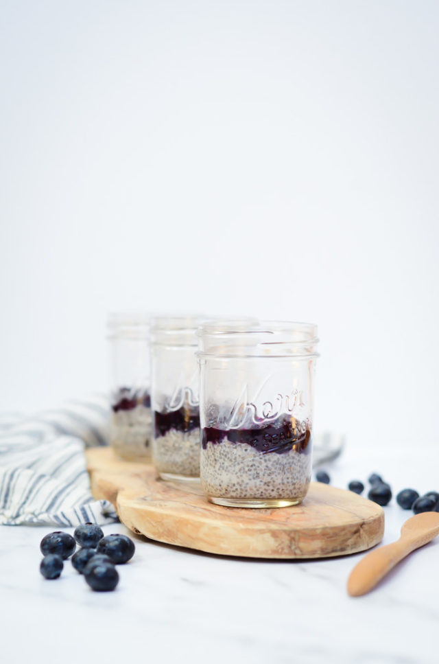 Three jars of Oat Milk Chia Pudding with Blueberry Orange Compote on a rustic wooden plank.