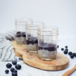 Three jars of Oat Milk Chia Pudding topped with Blueberry Orange Compote on a wooden serving plank.