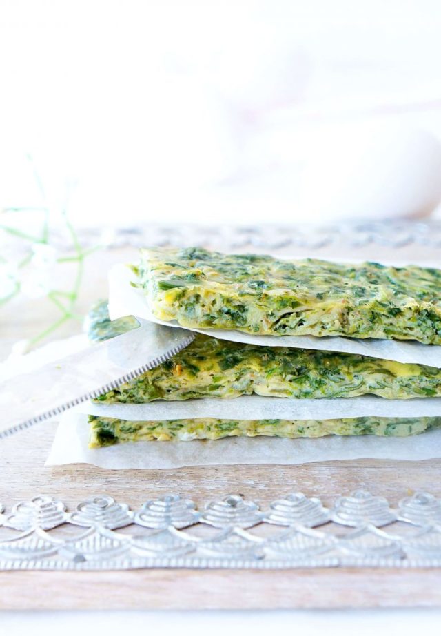 A stack of Spinach Zucchini Frittata Fingers separated by parchment paper and a butler knife.