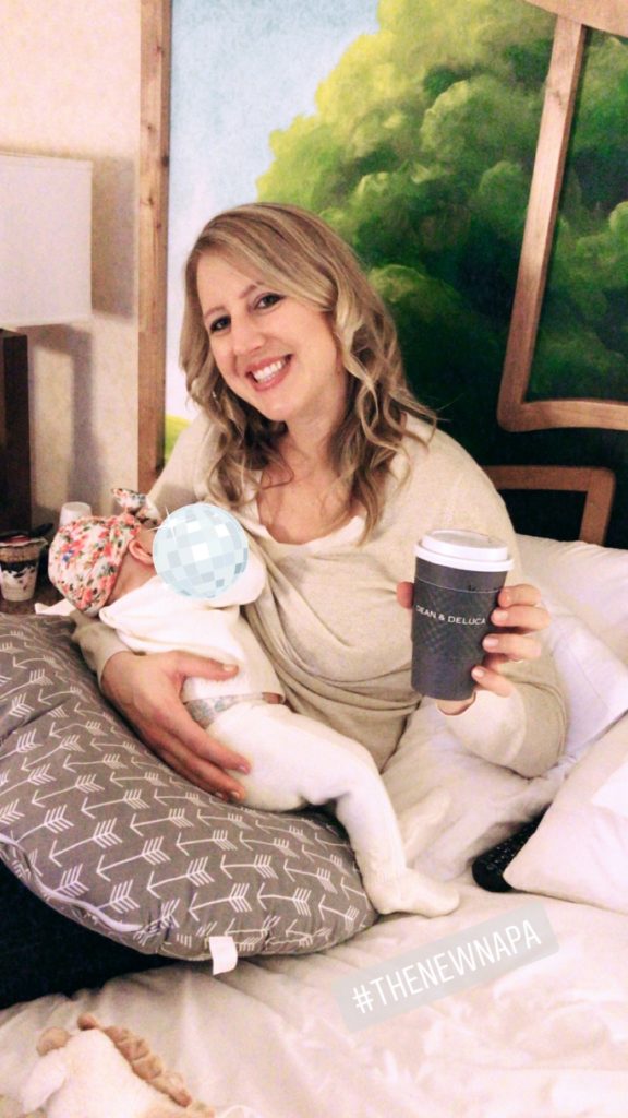 Mama breastfeeding her baby in bed with a cup of coffee in hand.