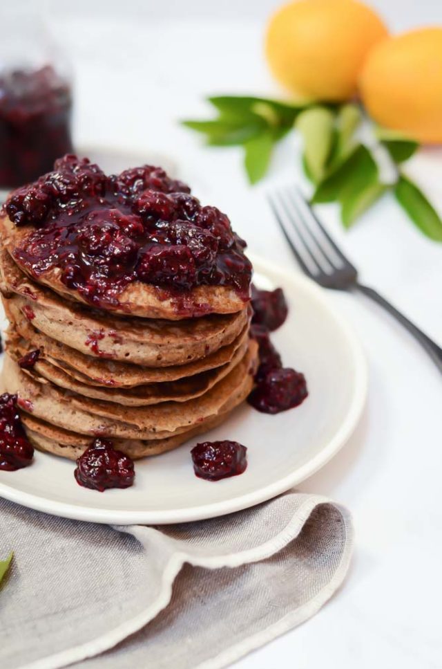 Side view of a fluffy stack of Lemon Vanilla Buckwheat Pancakes topped with a chunky blackberry syrup.