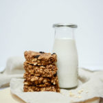 Four Peanut Butter Banana Breakfast Cookies stacked alongside a carafe of milk.