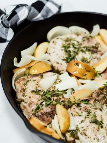 Another close-up look at Weeknight One-Pan Apple and Herb Pork Chops in a cast iron skillet with a black and white gingham napkin tied around the handle.