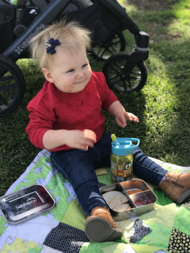 A happy toddler enjoying a lunch picnic on the grass. Picnics are a great thing to plan into your baby or toddler's meal plan!