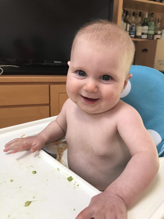 A cute baby stripped down in a highchair enjoying some of her first solid foods.