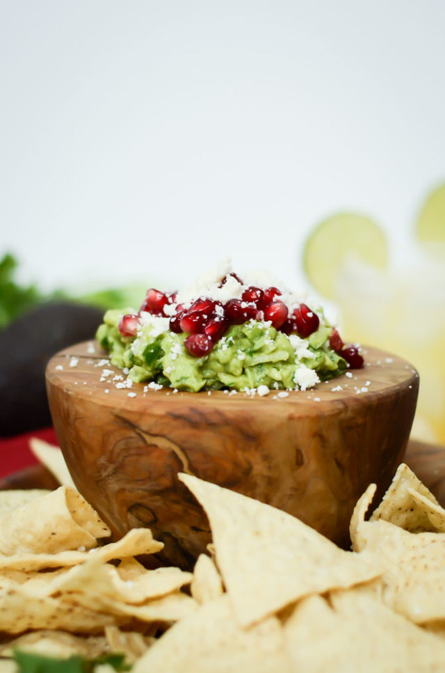 A wooden mortar filled with guacamole, surrounded by tortilla chips.