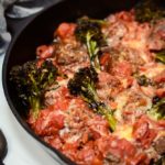 A close-up view of One-Pan Bison Meatballs with Broccolini and Tomato Sauce with some crusty bread in the background.