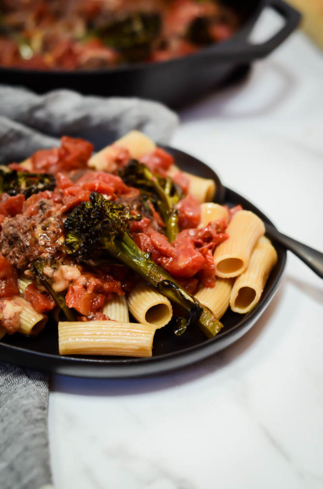 A plate of pasta topped with bison meatballs, broccolini and tomato sauce.