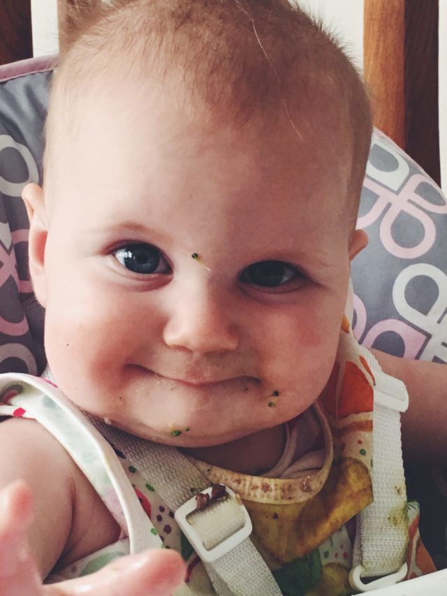 A baby with broccoli all over her face to help showcase the best vegetable preparations for baby-led weaning.