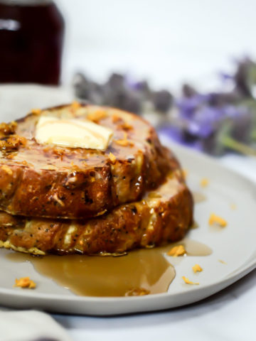 Two slices of lemon ricotta French toast are stacked on a plate, topped with a pat of butter and drizzled with syrup.