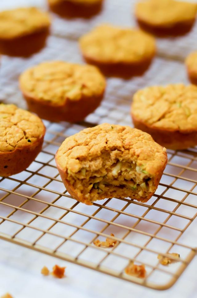 A rack of cooling Sweet Potato Zucchini Muffins shows one with a bite out of it. Vegetable-packed muffins are a great food for 18-month-olds.