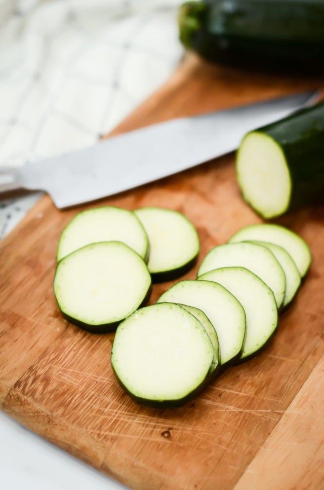 One zucchini partially sliced on a cutting board with a chef's knife in the background. Zucchini is a great vegetable for baby-led weaning!