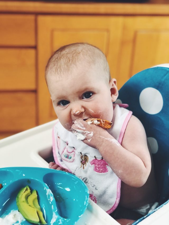 A baby girl in her high chair exploring some of her first solid foods.