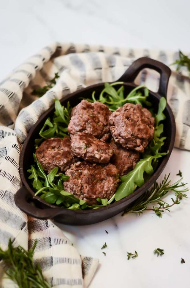 A cast iron dish filled with a bed of lettuce and topped with mushroom-beef sliders.