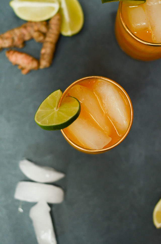 An overhead shot of a glass of tasty Pineapple Turmeric Ginger Elixir, surrounded by ice cubes and fresh ginger root.