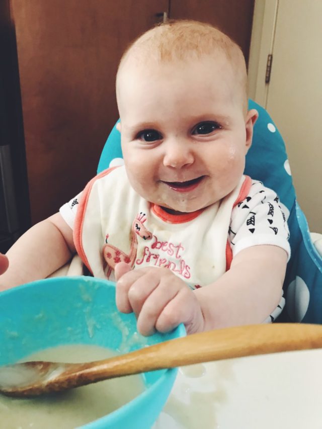 A baby enjoying her first taste of solid food in her highchair.