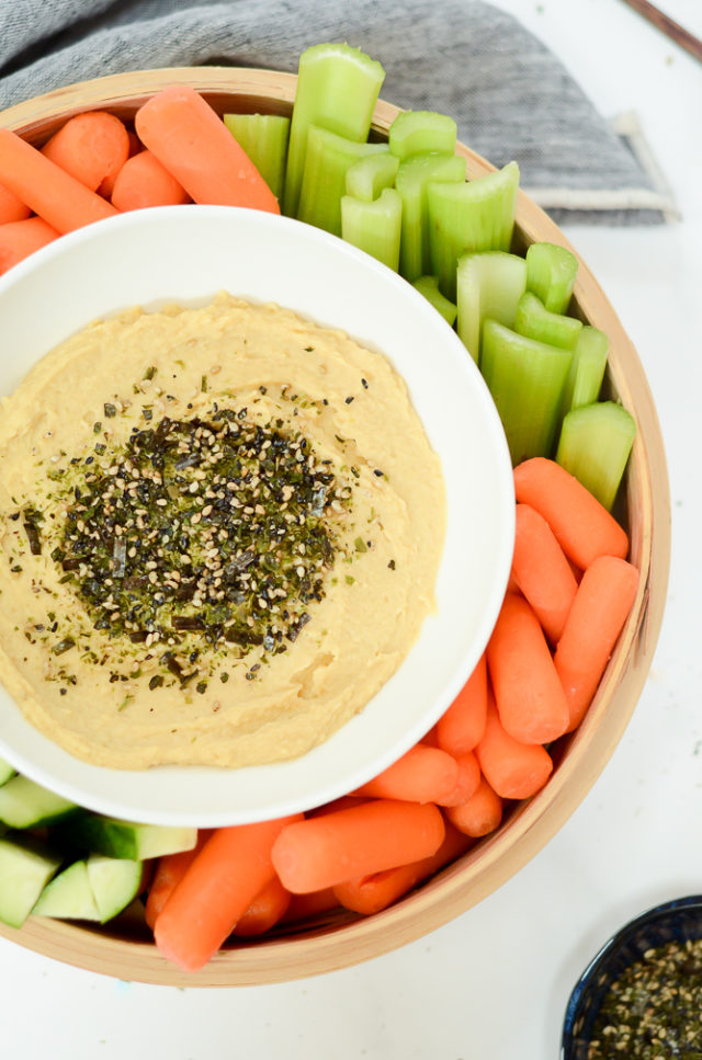 A bowl of Miso Furikake Hummus surrounded by fresh vegetables.