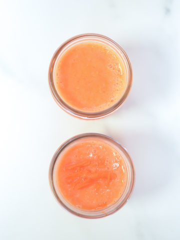 An overhead shot of two orange-carrot smoothies in Mason jars.