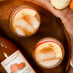 An overhead shot of two glasses of Pumpkin Apple Bourbon Smash on a wooden platter.