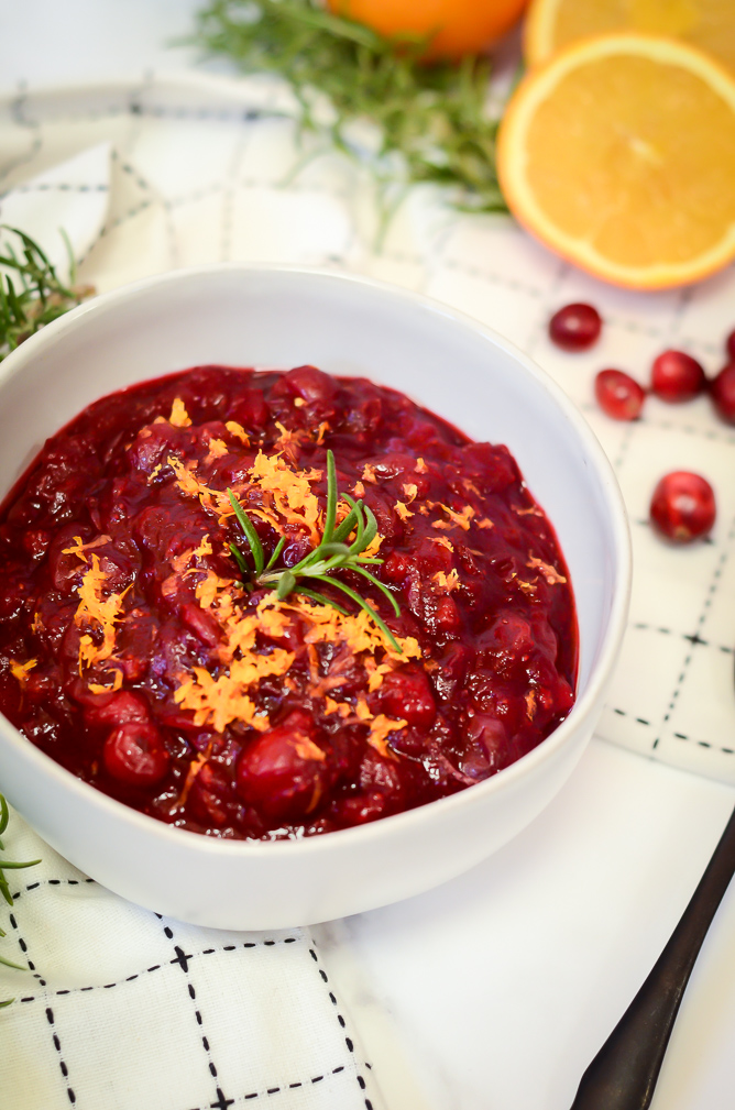 A bowl of cranberry sauce topped with orange zest and rosemary.