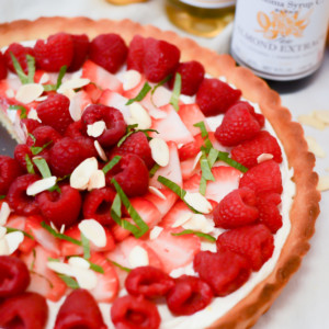 A Greek Yogurt Berry Tart with Almond Crust surrounded by bottles of almond extract and almond syrup, plus fresh lemons.