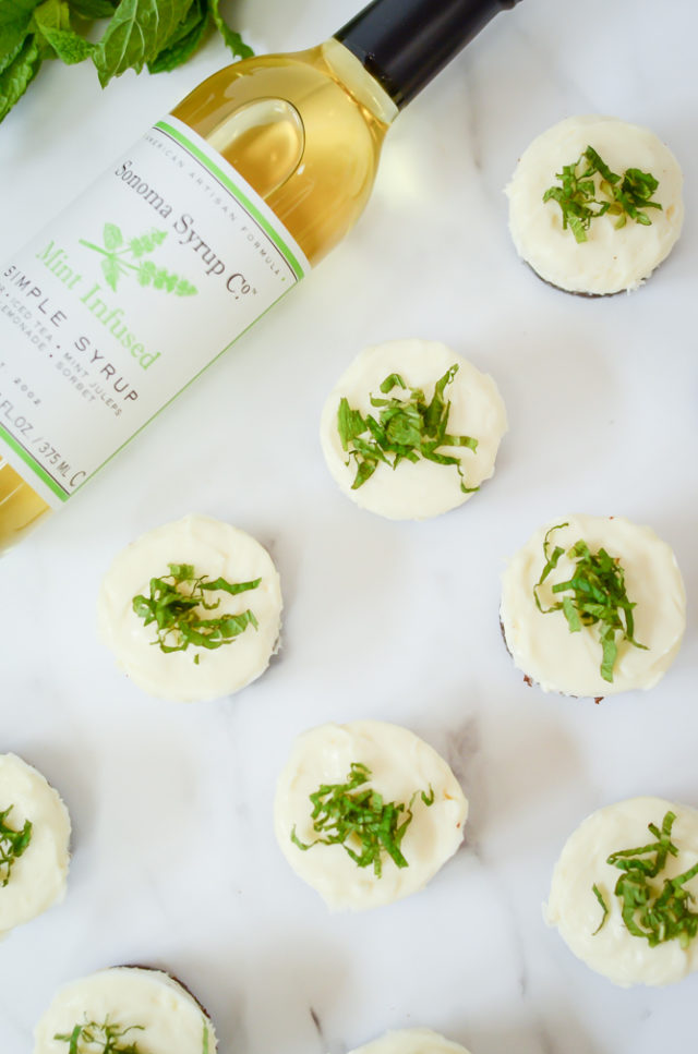 An overhead shot of a batch of Mini Fresh Mint Cheesecakes and a bottle of mint-infused simple syrup.