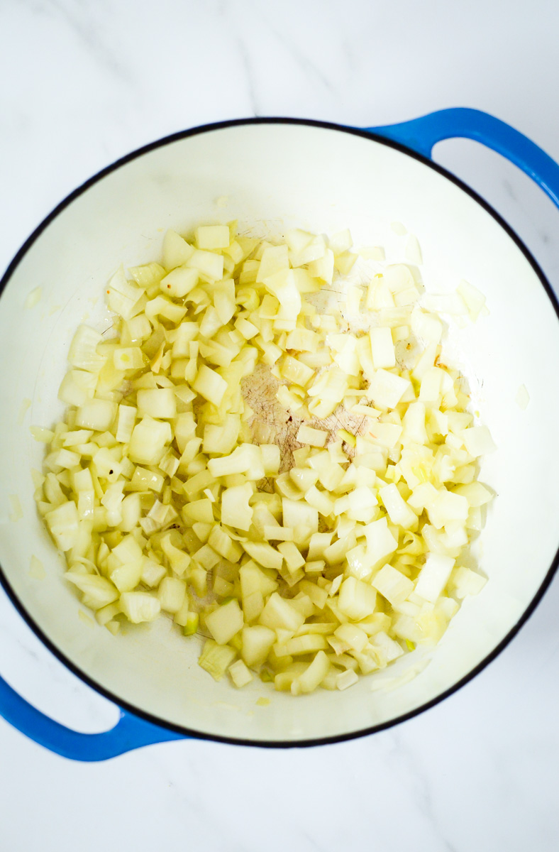 A diced onion being sauteed in olive oil in a Dutch oven.