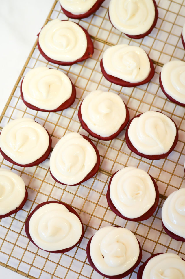 Red velvet cake cookies topped with peppermint cream on a cooling rack.