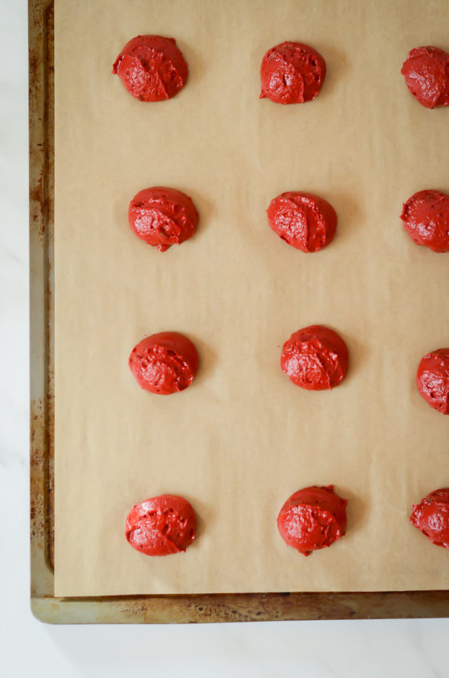 A cookie sheet with drops of red velvet cookie dough.