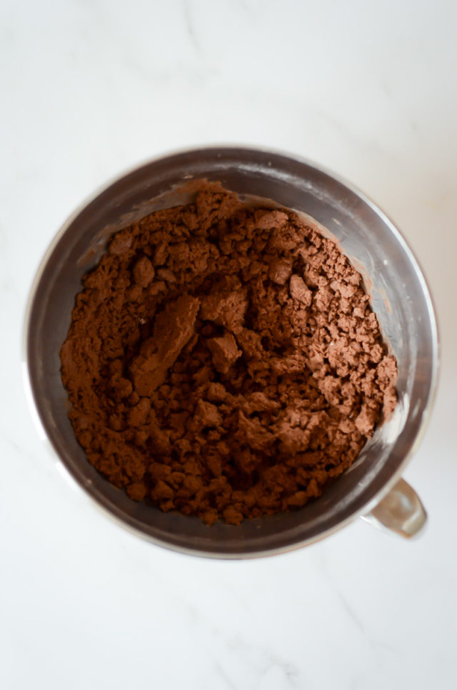 A metal mixing bowl filled with a crumbly chocolate dough.