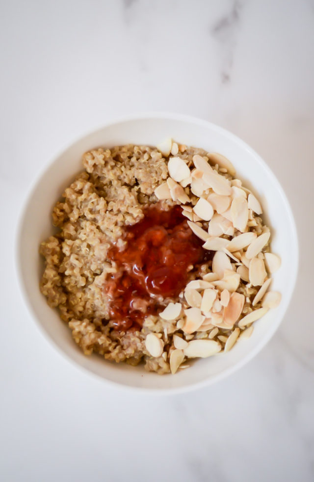 A bowl of quinoa topped with jam and sliced almonds.
