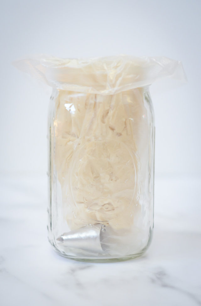 A piping bag of buttercream propped up in a Mason jar.