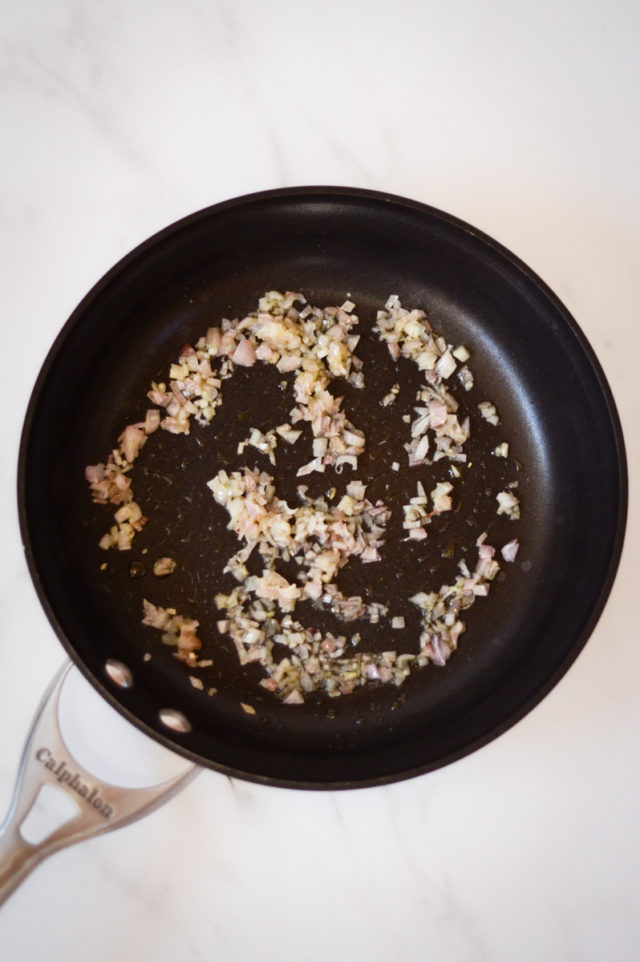 Minced shallots being sautéed in a frying pan.