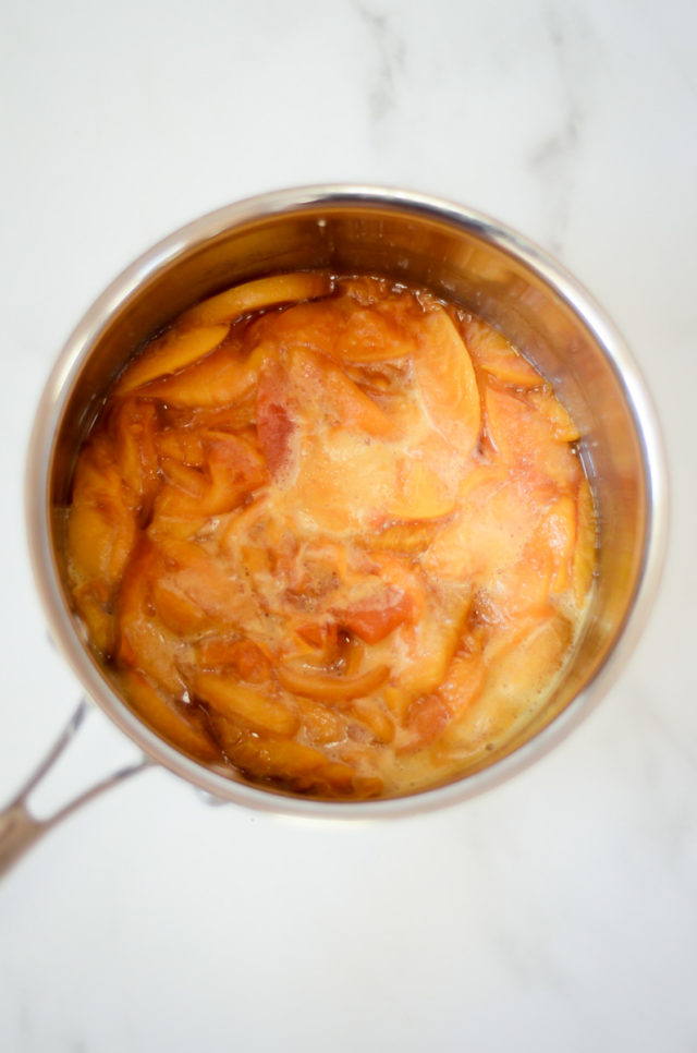 An overhead shot of a saucepan of simmering peaches.