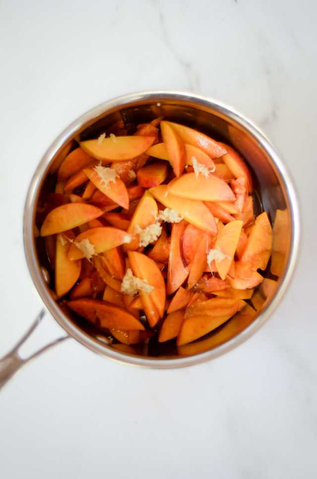 An overhead shot of a saucepan full of peaches and fresh ginger.